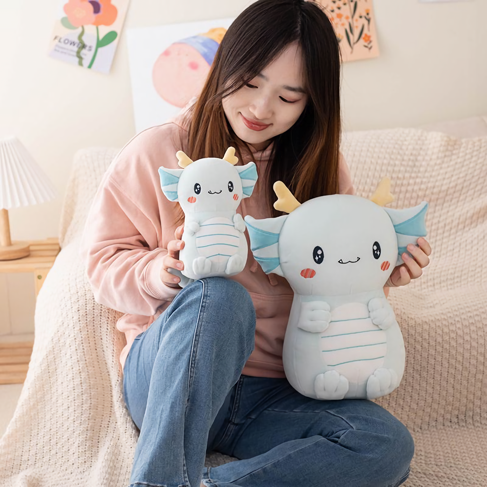 Girl on a sofa holding two light blue axolotl dragon plushies of different sizes
