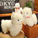 Large white alpaca plush and a smaller white alpaca plush with red collars on a wicker mat