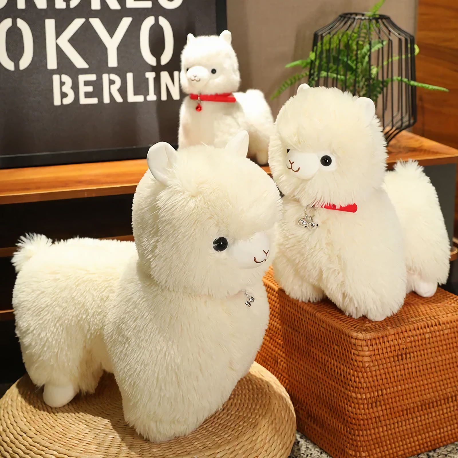 Large white alpaca plush and a smaller white alpaca plush with red collars on a wicker mat