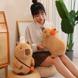 Woman sitting on the floor with a capybara plush on her lap beside a capybara with a duck