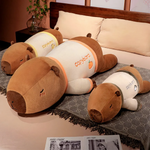 Three lying capybara plush pillows with orange, yellow and green trim on a bed