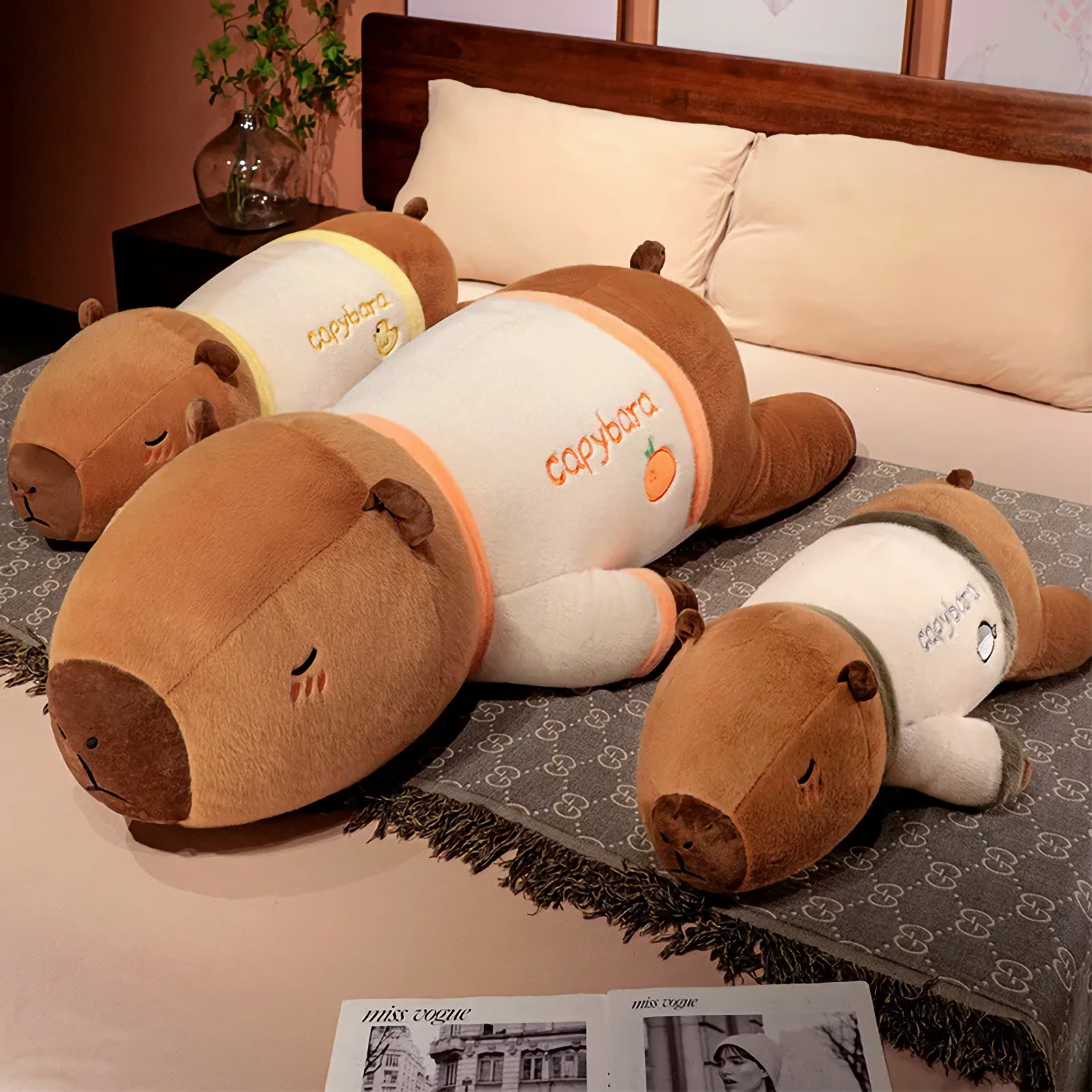 Three lying capybara plush pillows with orange, yellow and green trim on a bed