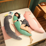 Woman sleeping on a bed between curved gray sea lion, green dinosaur and pink unicorn plush pillows
