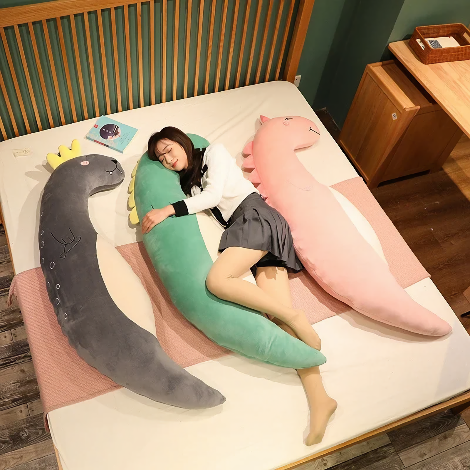 Woman sleeping on a bed between curved gray sea lion, green dinosaur and pink unicorn plush pillows