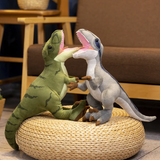 Green Tyrannosaurus Rex and gray Velociraptor plush toys on a woven pouf, facing each other with open mouths.