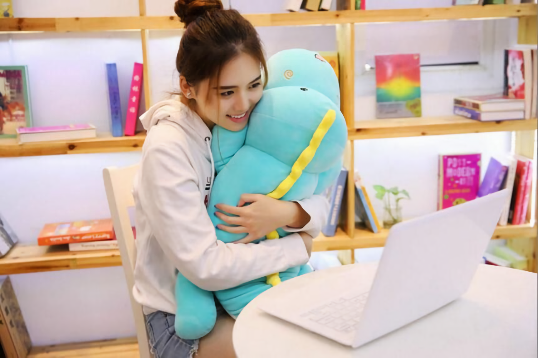 Woman smiling while hugging a long blue dinosaur plush with a yellow back ridge