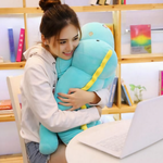 Woman smiling while hugging a long blue dinosaur plush with a yellow back ridge