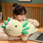 Girl smiling at a laptop on a wooden desk with a green axolotl plush lying beside her