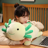 Girl smiling at a laptop on a wooden desk with a green axolotl plush lying beside her