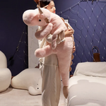 Woman hugging a large pink and white dragon plush body pillow in a cozy room.