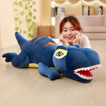 Woman lying on the floor smiling beside a long blue T-Rex plush pillow
