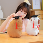 Woman resting her chin on a desk beside a brown and a white graduation capybara plush