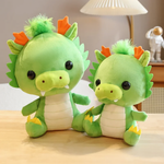 Two green dragon plush toys with orange horns on a table; one larger than the other.
