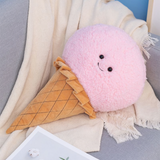 Pink ice cream cone plush pillow with a smiling face on a sofa with a cream blanket