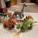 Triceratops plush and Stegosaurus plush on carpet, with gift boxes behind and Brontosaurus plush on a table.