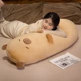 Woman lying on a bed with her head on a tan capybara bolster pillow