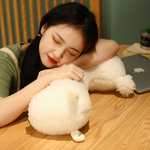 Woman sleeping with her head on a white alpaca plush on a wooden desk
