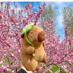 Lotus leaf capybara plush among pink blossoms outdoors