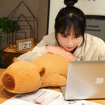 Woman lying on a desk with her head on a lying capybara plush pillow and a laptop
