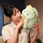 Woman holding a green pig-dragon plush with a small snout and tiny horns, gently touching its nose.