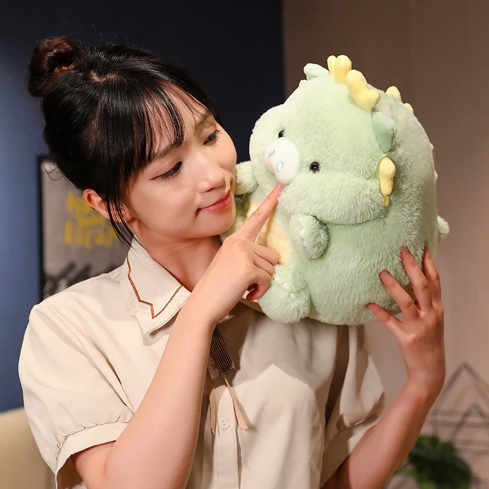 Woman holding a green pig-dragon plush with a small snout and tiny horns, gently touching its nose.