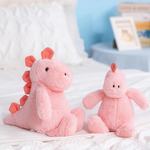 Two pink dinosaur plush toys sitting on a bed with a photo frame