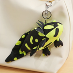Black and lime green spotted axolotl plush with a clip ring hanging from a white bag