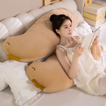 Woman reading a book on a bed beside long tan capybara body pillows