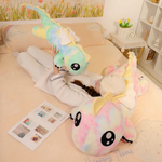 Woman hugging a blue rainbow winged dragon plush on a pastel bed
