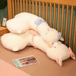 Two long white alpaca plush pillows with blue and pink bows lying on a bed