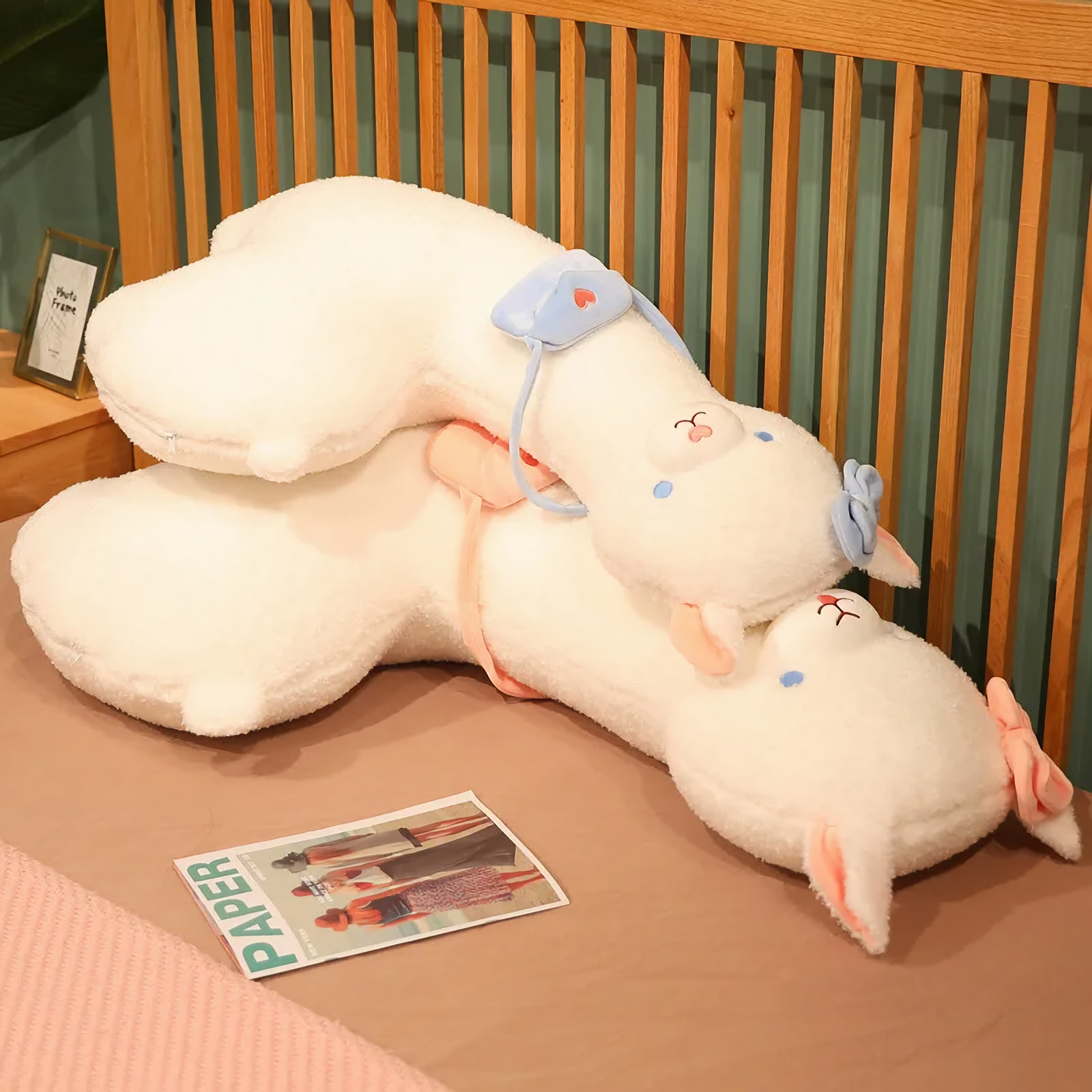 Two long white alpaca plush pillows with blue and pink bows lying on a bed