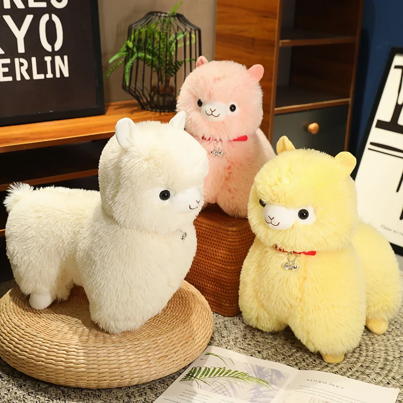 White and yellow alpaca plushies with a pink one behind them on a cozy shelf