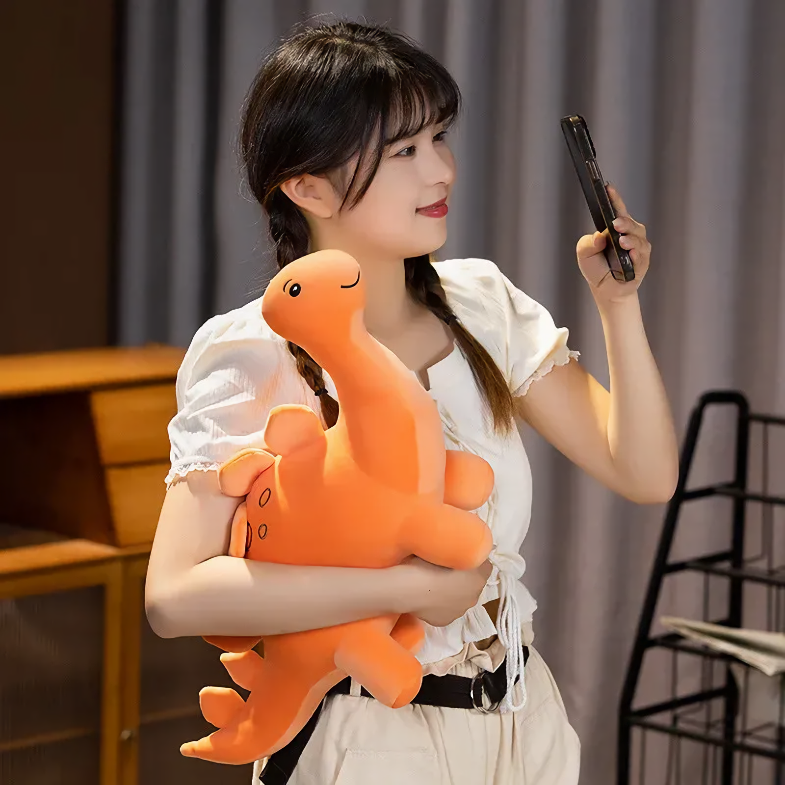 Woman holding orange Stegosaurus plush, looking at something off-camera.