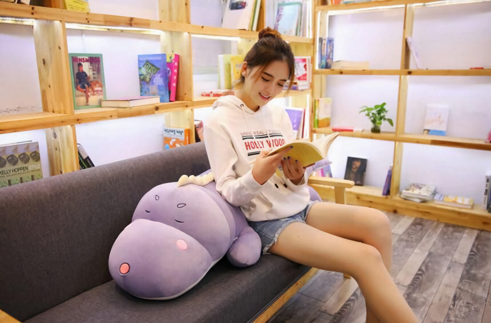 Woman sitting on a sofa reading with a purple dinosaur plush pillow on her lap