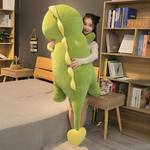A woman hugging a large green dinosaur plush with yellow spikes next to a bed and bookshelf.