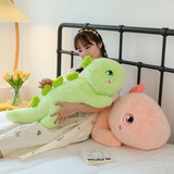 Woman holding green dinosaur plush pillow, pink plush beside, on a bed.