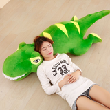 Woman lying on the floor resting her head on a long green T-Rex plush pillow