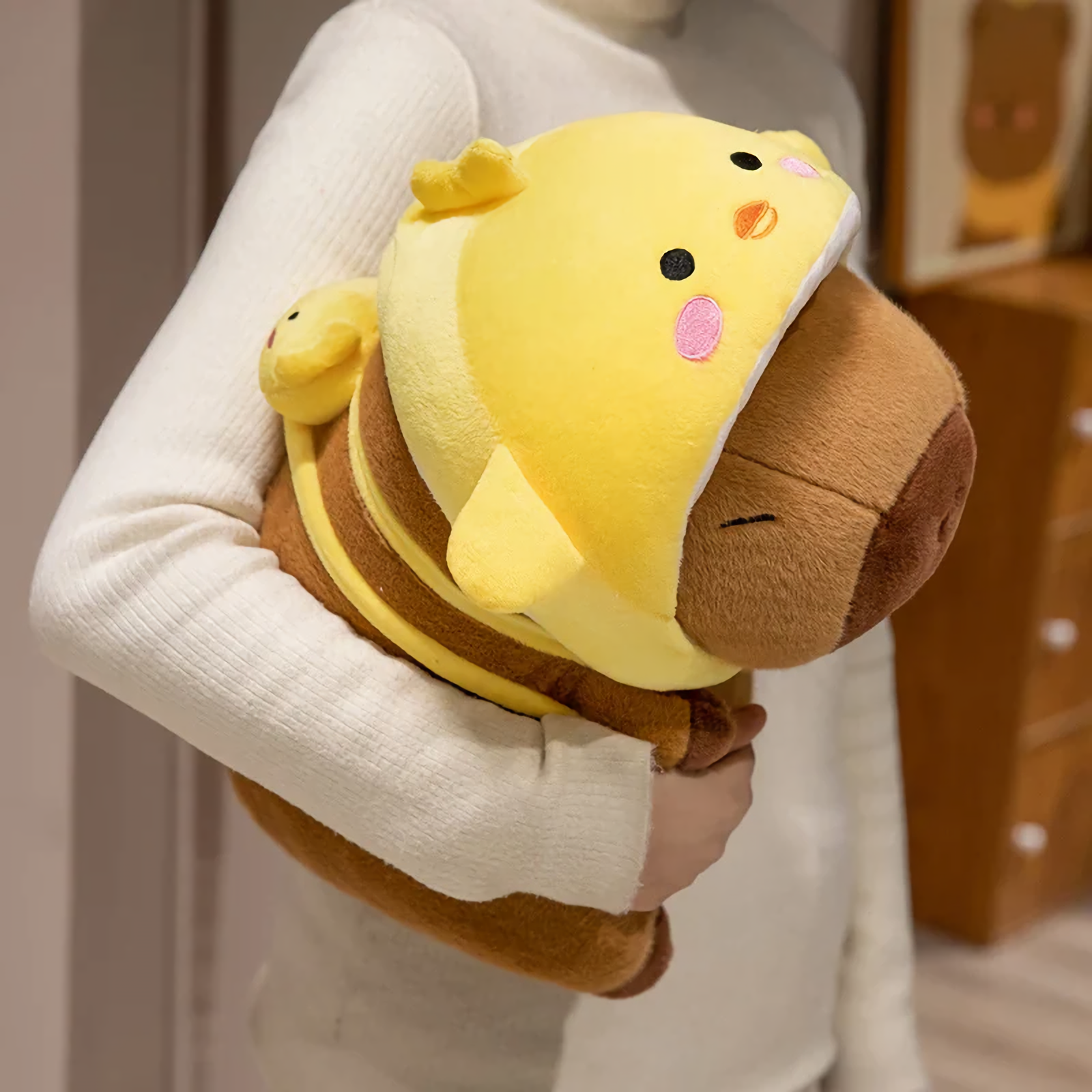 Woman hugging a capybara plush in a yellow chick hood