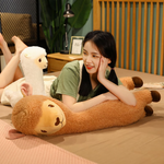 Woman lying on a bed beside a long brown alpaca plush and a white one