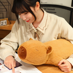 Woman reading beside a lying capybara plush pillow on a desk