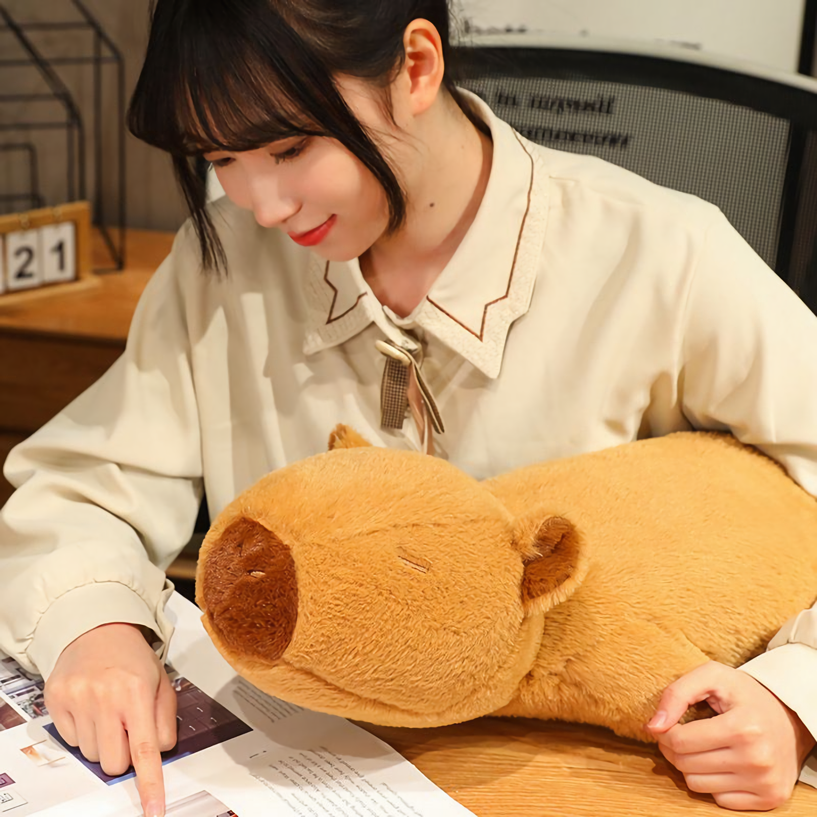 Woman reading beside a lying capybara plush pillow on a desk