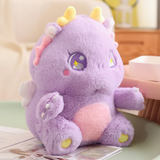Purple baby dragon plush with golden horns and sparkly star eyes sitting on a table with a book beside it.