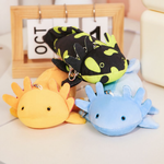 Yellow, blue and spotted green axolotl plushies on a white table beside a calendar