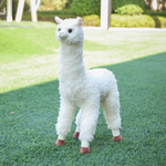 White standing alpaca plush with curly fur on a green lawn