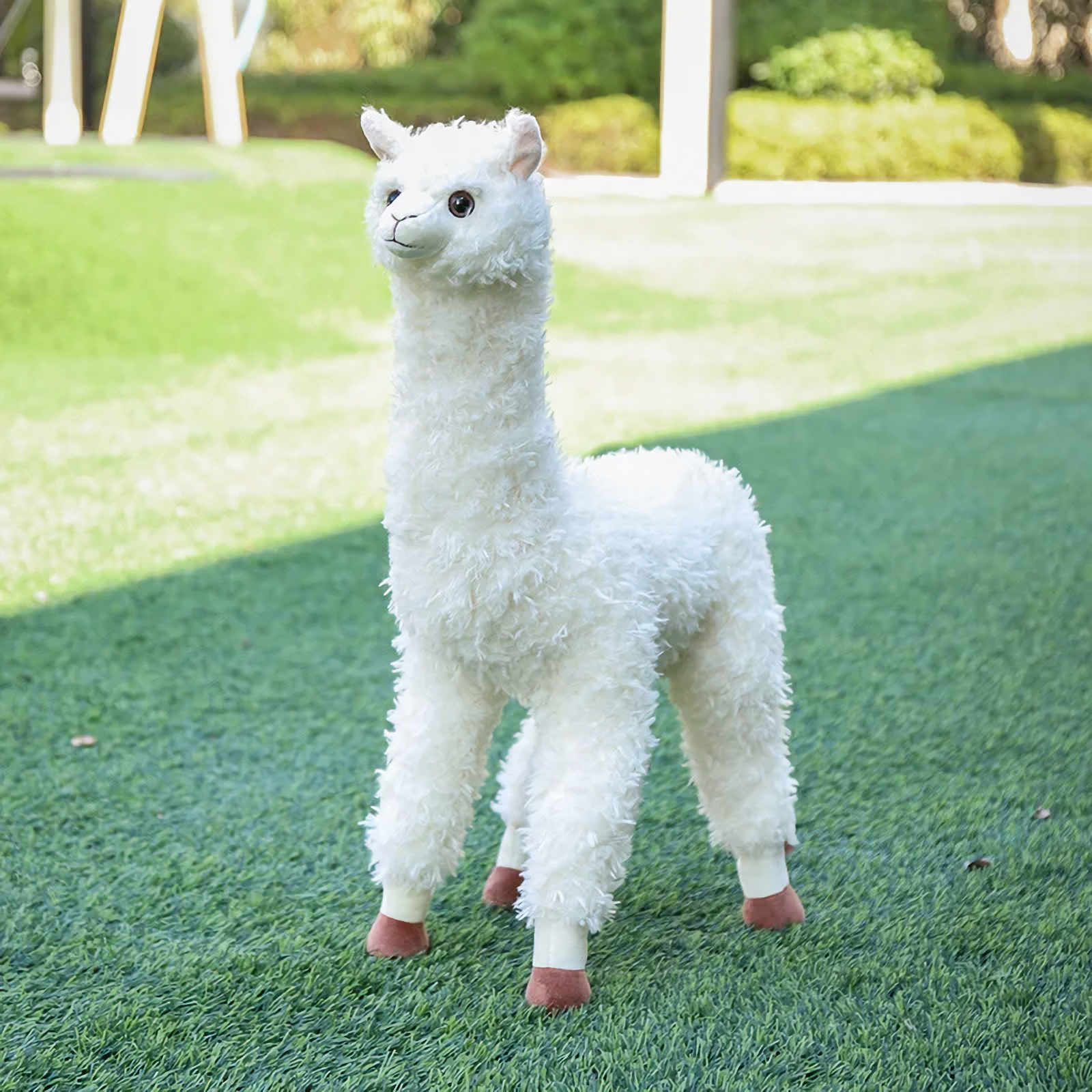 White standing alpaca plush with curly fur on a green lawn