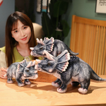 Woman with three gray Triceratops plush toys on a table, each a different size.