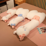 Three long white alpaca plush pillows with bows lying on a pink bedsheet