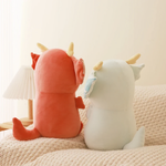 Back view of a burgundy and a light blue axolotl dragon plush with tails on a sofa
