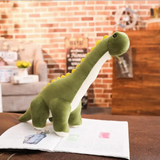 Green Brachiosaurus dinosaur plush with cream belly on a sofa next to an open book in a cozy room.