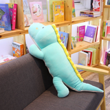 Long blue dinosaur plush body pillow leaning against a dark sofa in a bright room